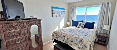 A bedroom with a bed, a television on a dresser, a window with curtains, and a painting on the wall.