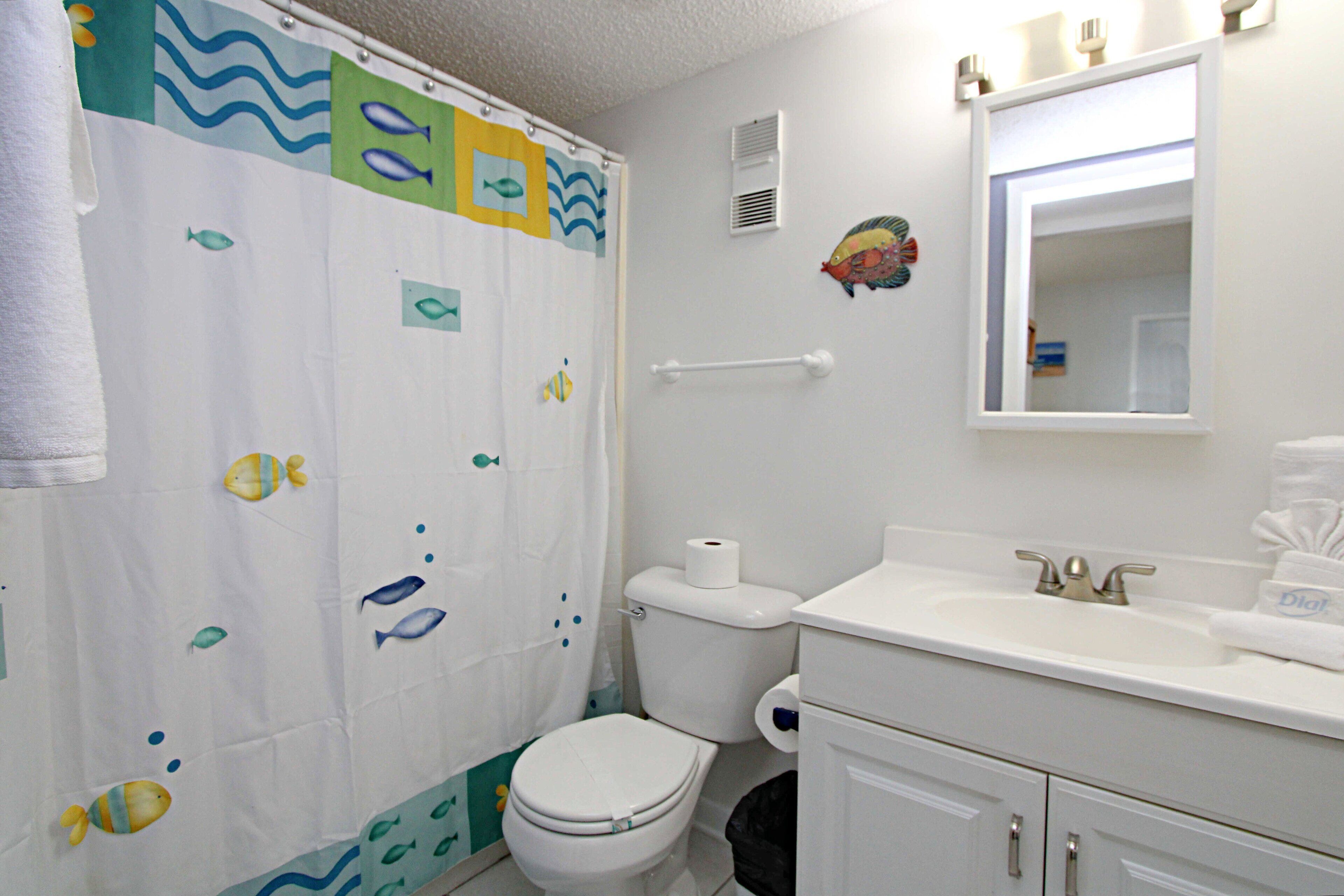 Ein Badezimmer mit Duschvorhang mit Fischmotiven, Toilette, Waschbecken mit Spiegel und Handtuchhalter.