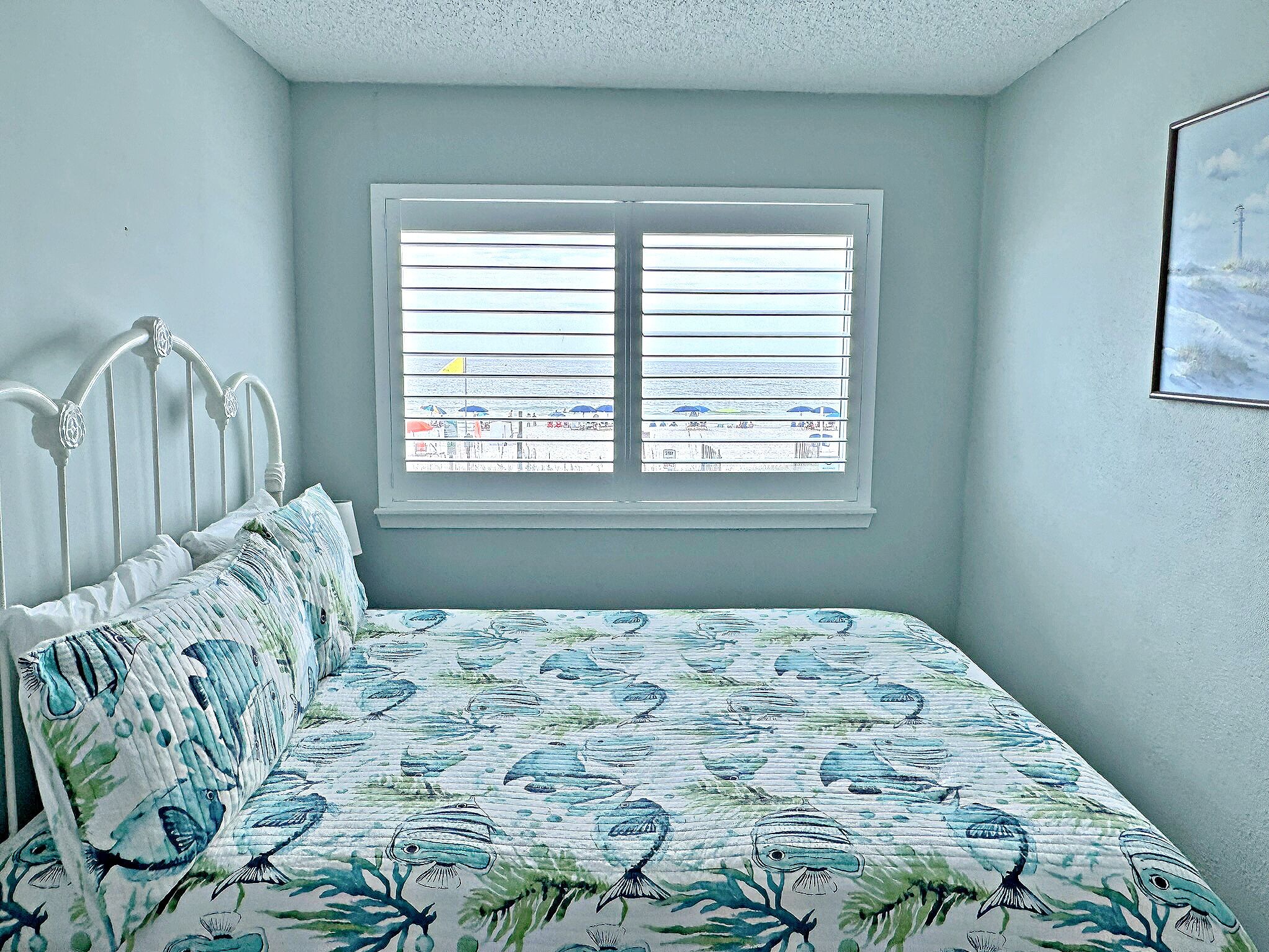 A bedroom with a bed, a window with blinds, and a painting on the wall.