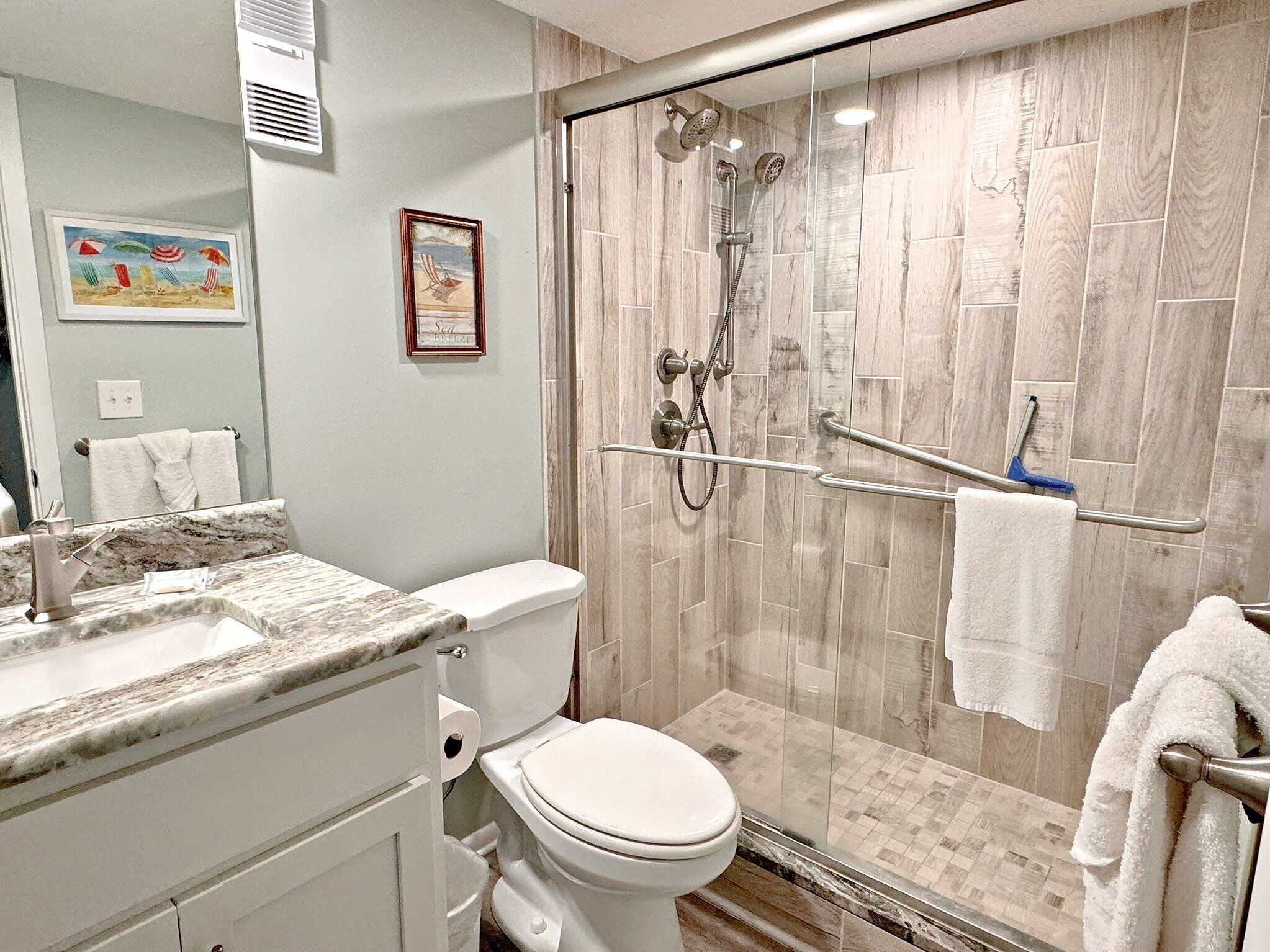 A modern bathroom with a glass-enclosed shower, a toilet, and a vanity with a marble countertop.