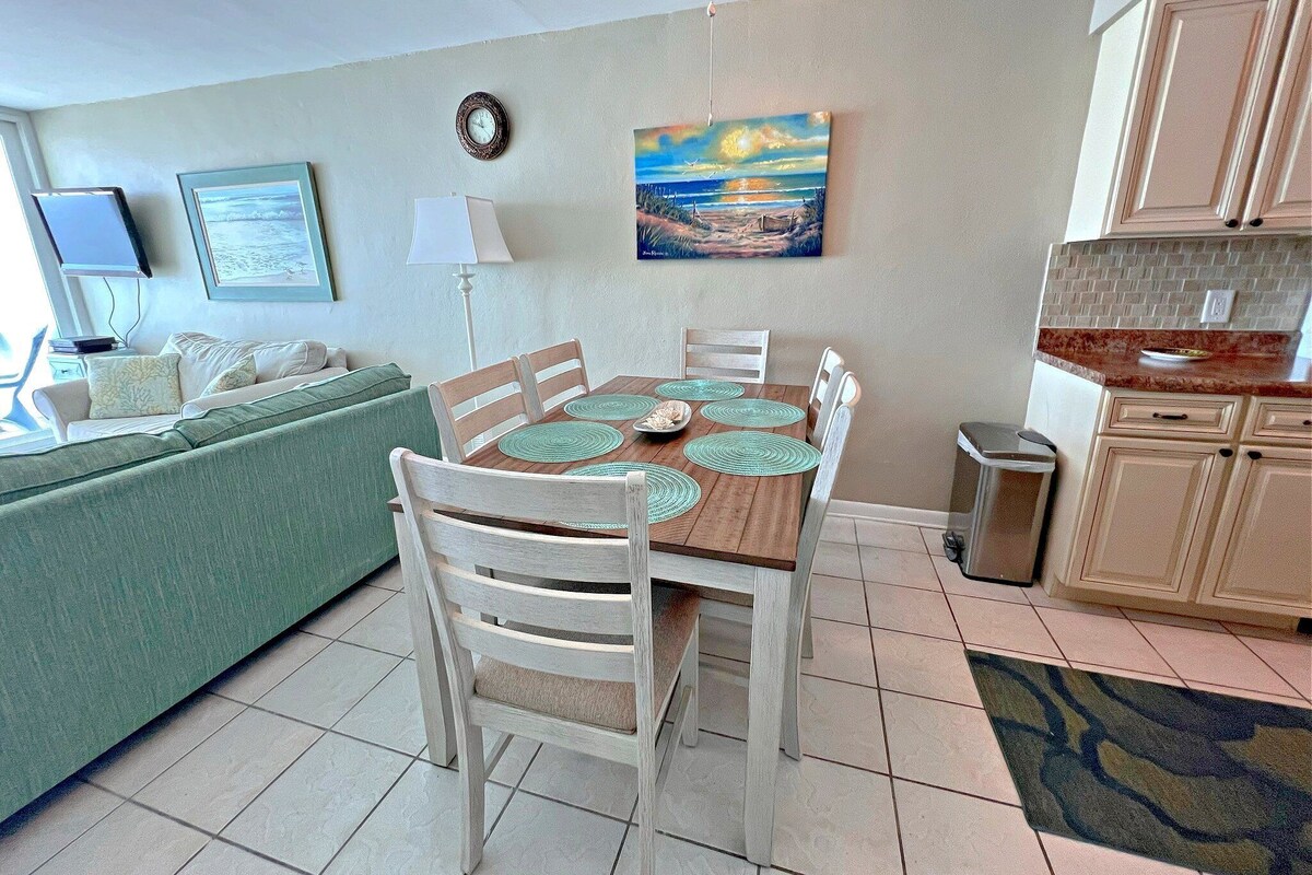 A dining area with a wooden table, white chairs, and a painting above.