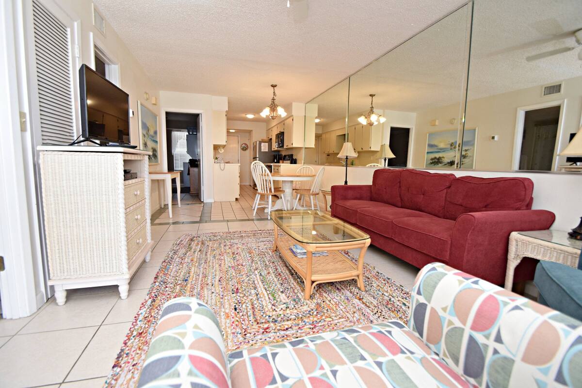 A living room with a red sofa, a glass coffee table, and a patterned rug.