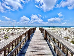 Een houten looppad dat naar een strand leidt met wit zand en een helderblauwe lucht.