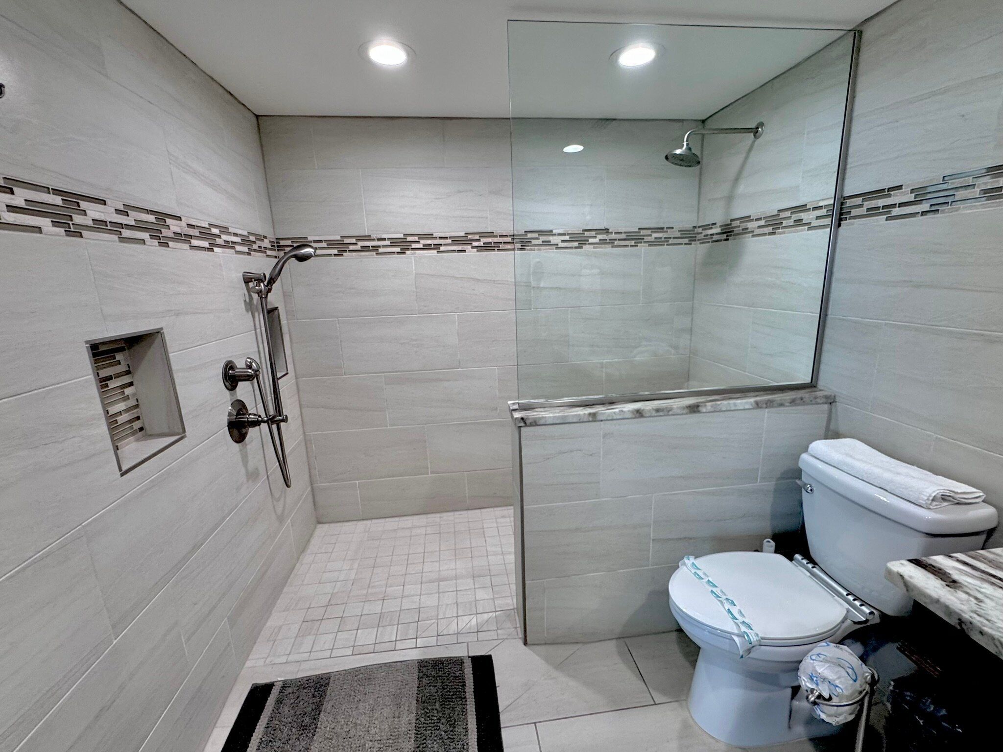 Ein modernes Badezimmer mit einer Glaskabine zur Dusche, einer Toilette mit Deckel und einem Waschbecken.