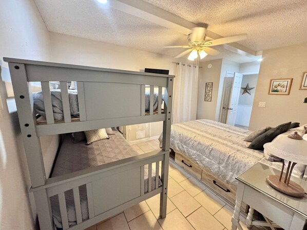 A bedroom with a bunk bed, a single bed, a ceiling fan, and a bedside table.