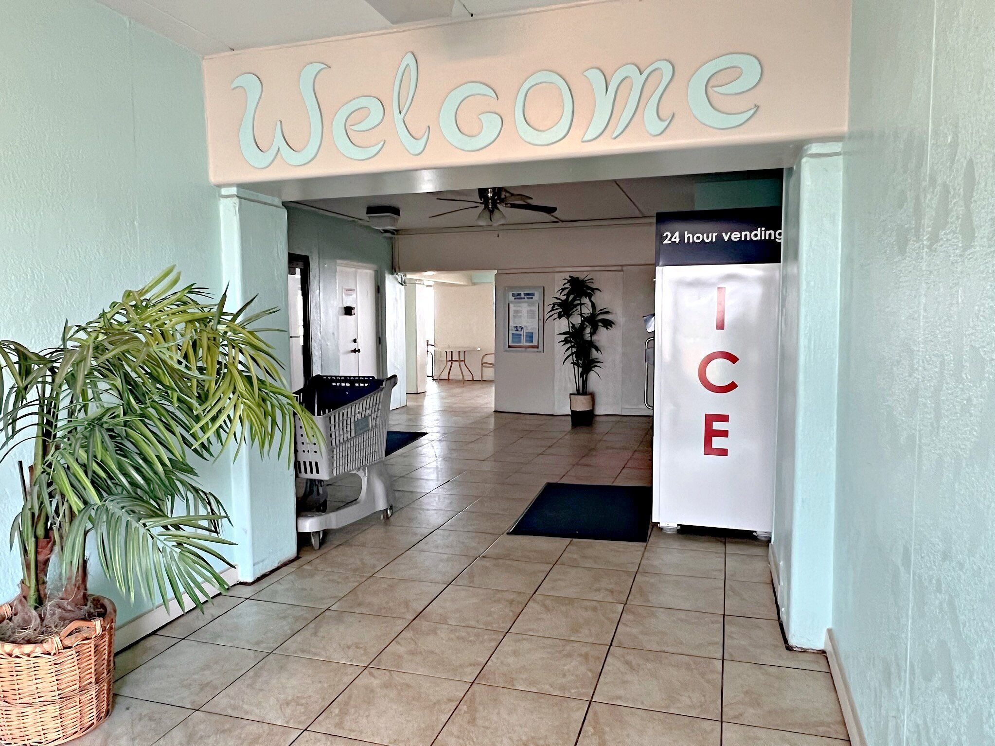 A hotel lobby with a 'Welcome' sign, a 24-hour ice machine, and a potted plant.