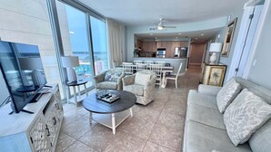 A spacious living area with a large TV, comfortable seating, a dining area, and a kitchen. - Island Tower (Gulf Shores)