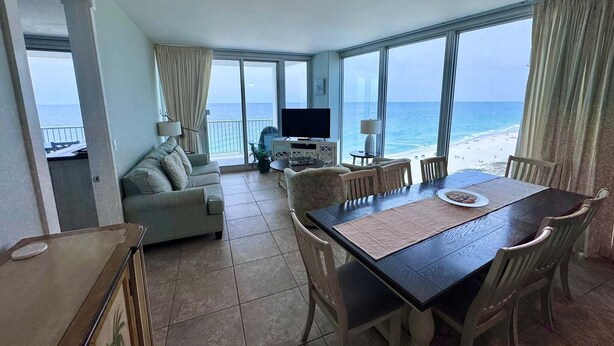 A room with a balcony, a dining table, a sofa, and a TV. - Island Tower (Gulf Shores)