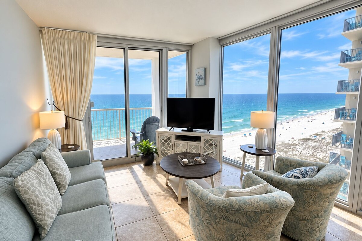 A balcony with a TV, seating area, and a view of the beach.
