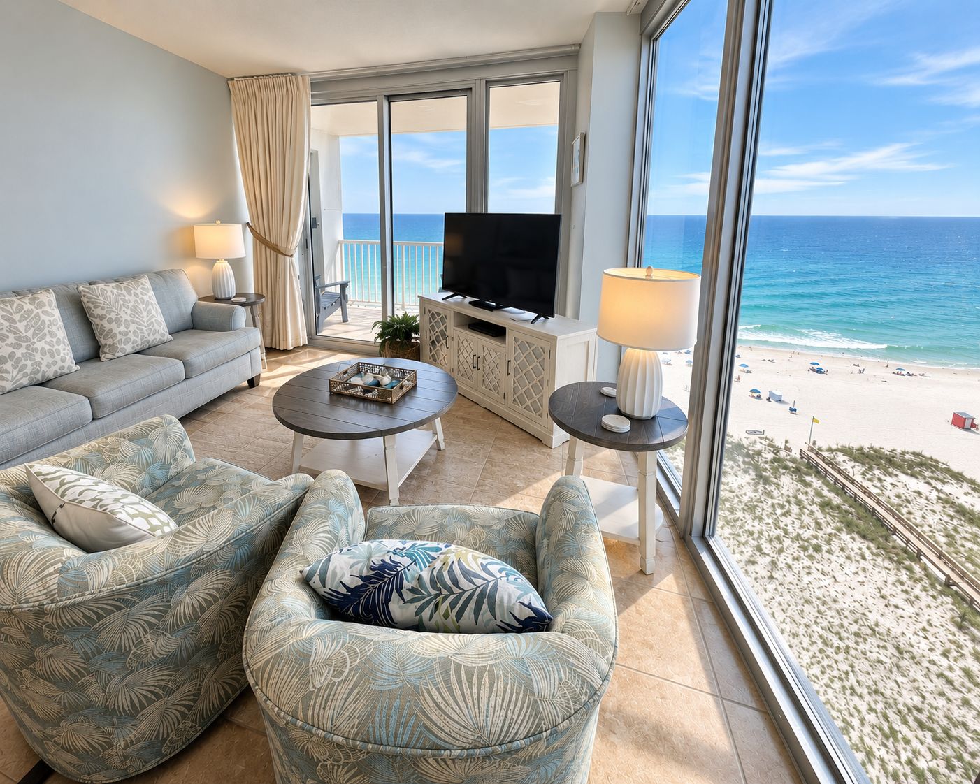 Un salon comprenant un canapé, un fauteuil et une table basse, une télévision, et donnant sur la plage.