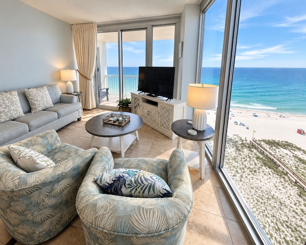Una sala de estar con sofá, sillón, mesa de centro, televisor y vista a la playa.
