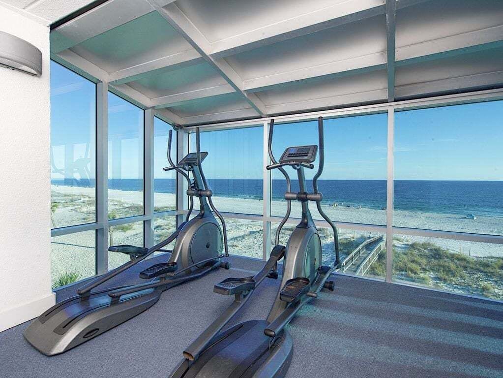 A gym with two stationary bikes and a treadmill, overlooking a beach.
