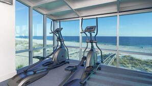 A gym with two stationary bikes and a treadmill, overlooking a beach. - Island Tower (Gulf Shores)