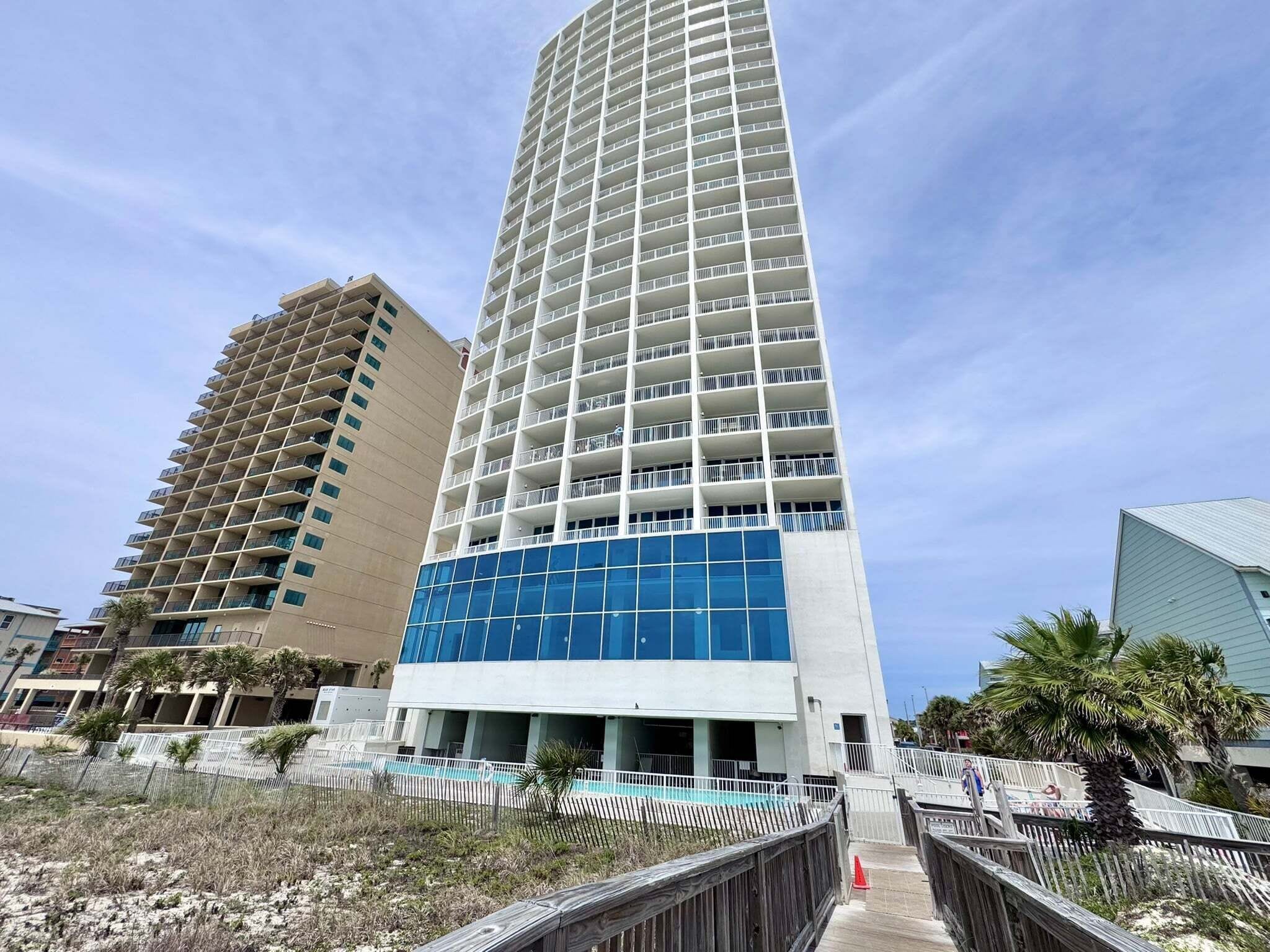 A tall hotel with multiple floors, a blue glass facade, and a pool area.