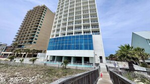 A tall hotel with multiple floors, a blue glass facade, and a pool area. - Island Tower (Gulf Shores)