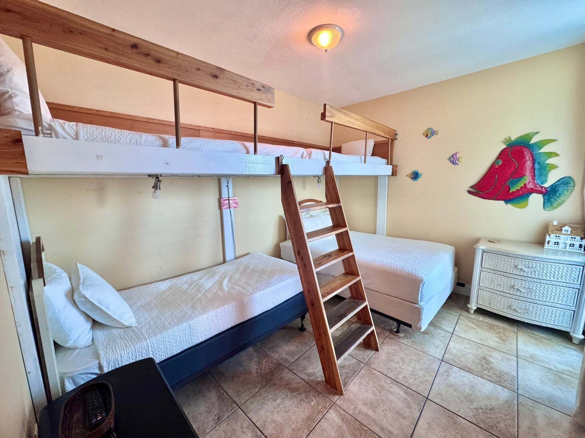 A bunk bed room with a ladder, a small dresser, and a wall decoration.