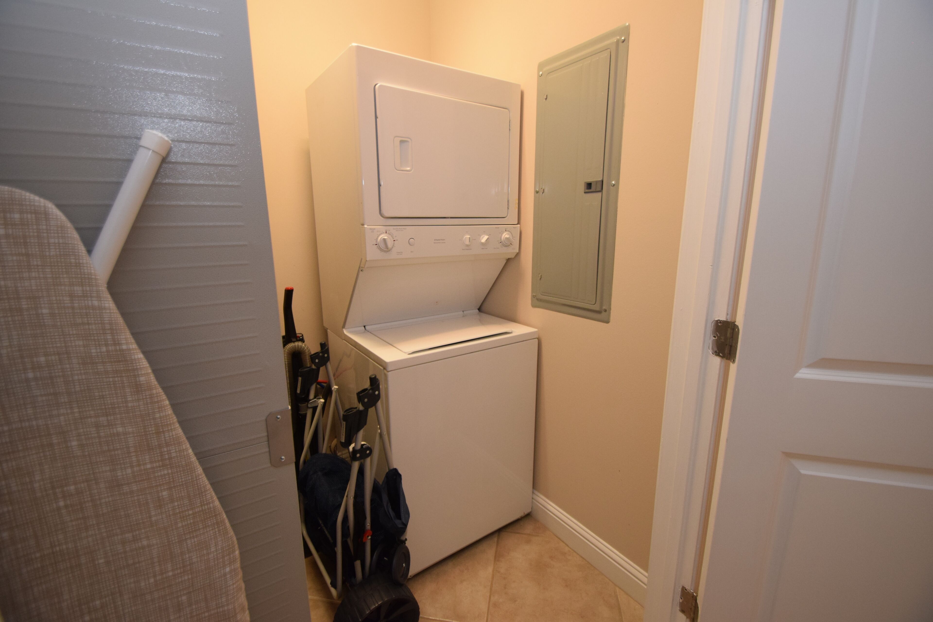 A laundry room with a stacked washer and dryer, a utility cart, and a door to another room.