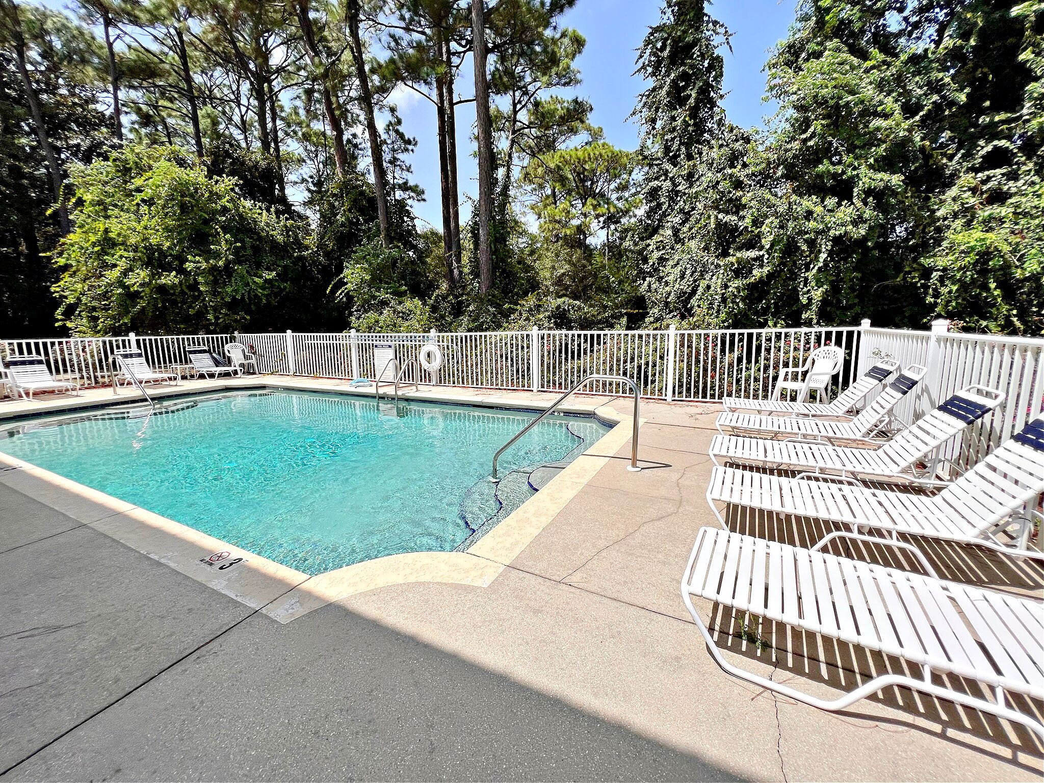 A swimming pool with white lounge chairs and a white fence.
