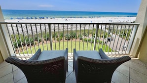 Ein Balkon mit Korbstühlen mit Blick auf einen Strand mit Sonnenschirmen und Menschen.