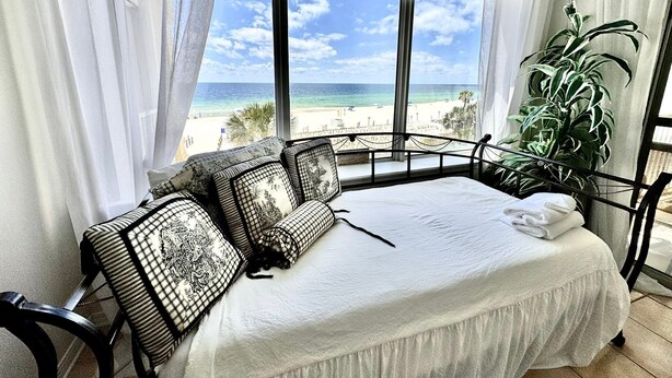 Ein Schlafzimmer mit Bett, Blick auf den Strand und einer Zimmerpflanze.