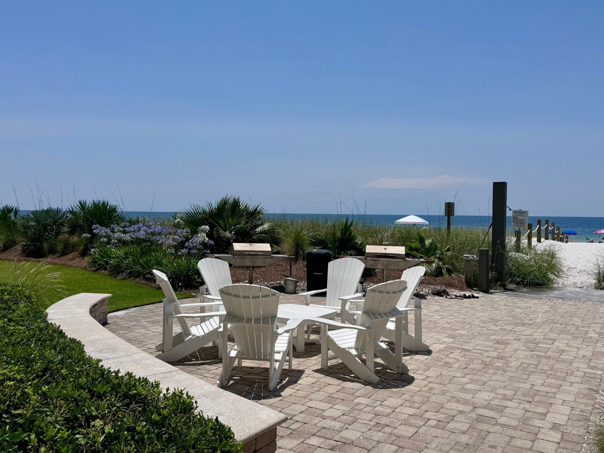 Un patio con sillas Adirondack, una parrilla y vistas a la playa.