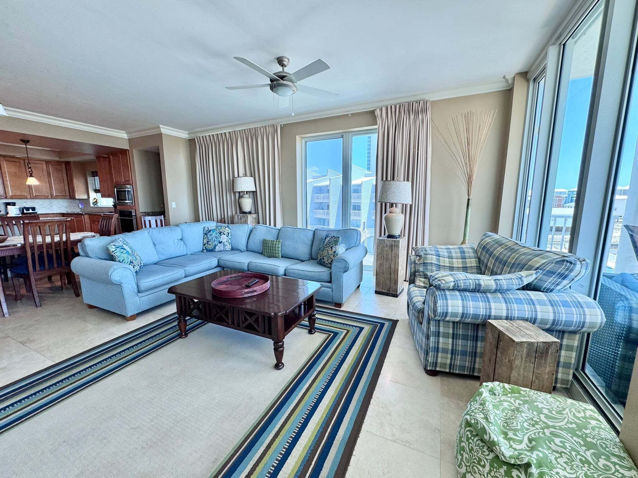 A living room with a sectional sofa, a plaid sofa, a coffee table, and a view of the city through large windows.