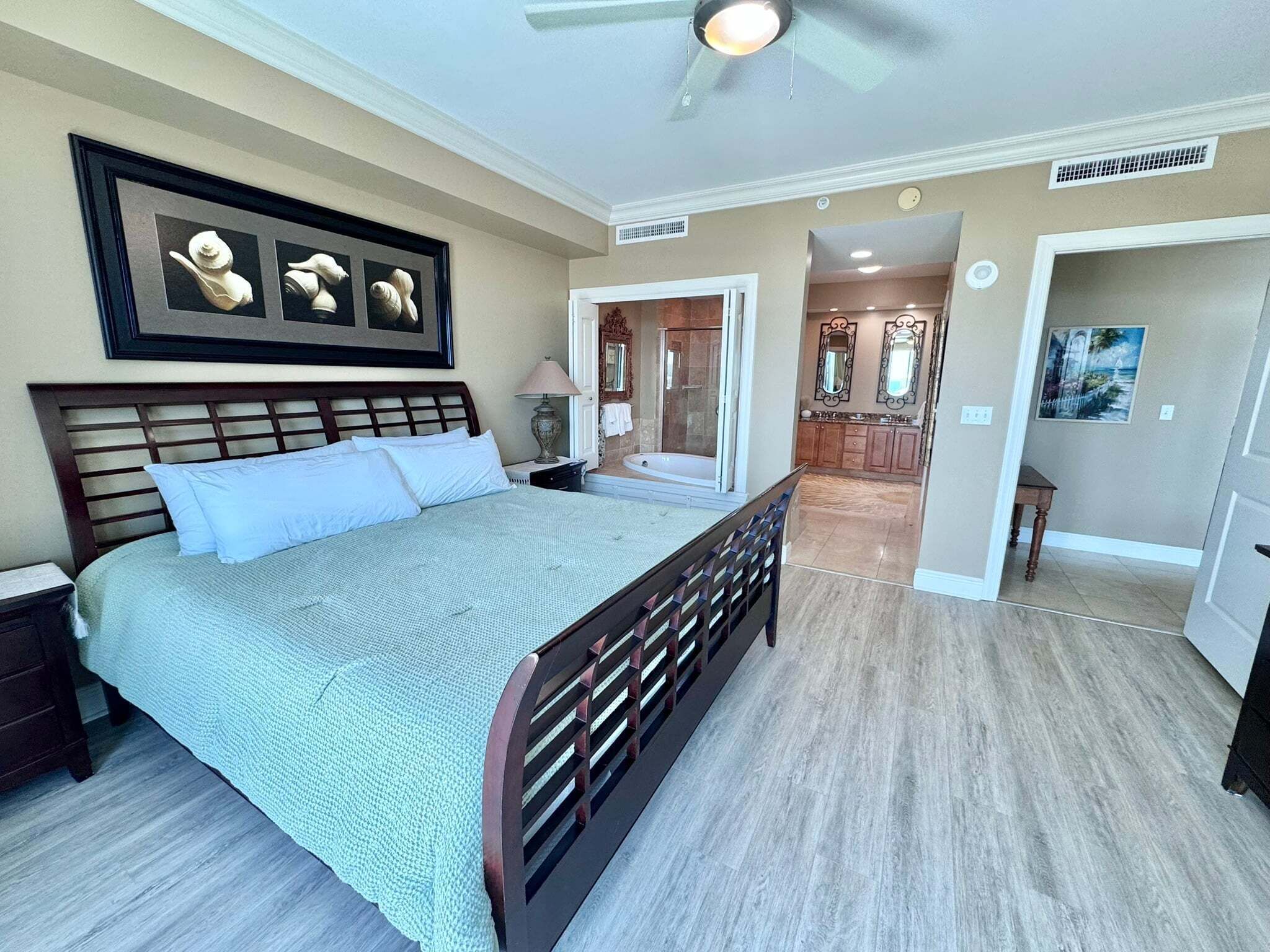 A bedroom with a bed, a nightstand, a bedside table, a ceiling fan, and a bathroom with a shower and a bathtub.