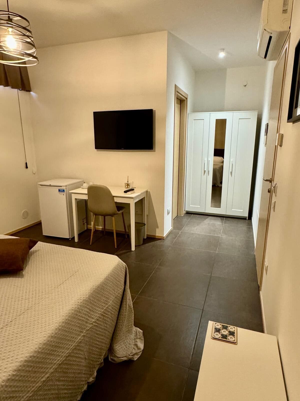 A compact hotel room with a bed, a desk, a chair, a television, and a wardrobe.