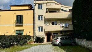 A multi-story residential building with a paved driveway and a parked car. - Il Ruggi  (Salerno)