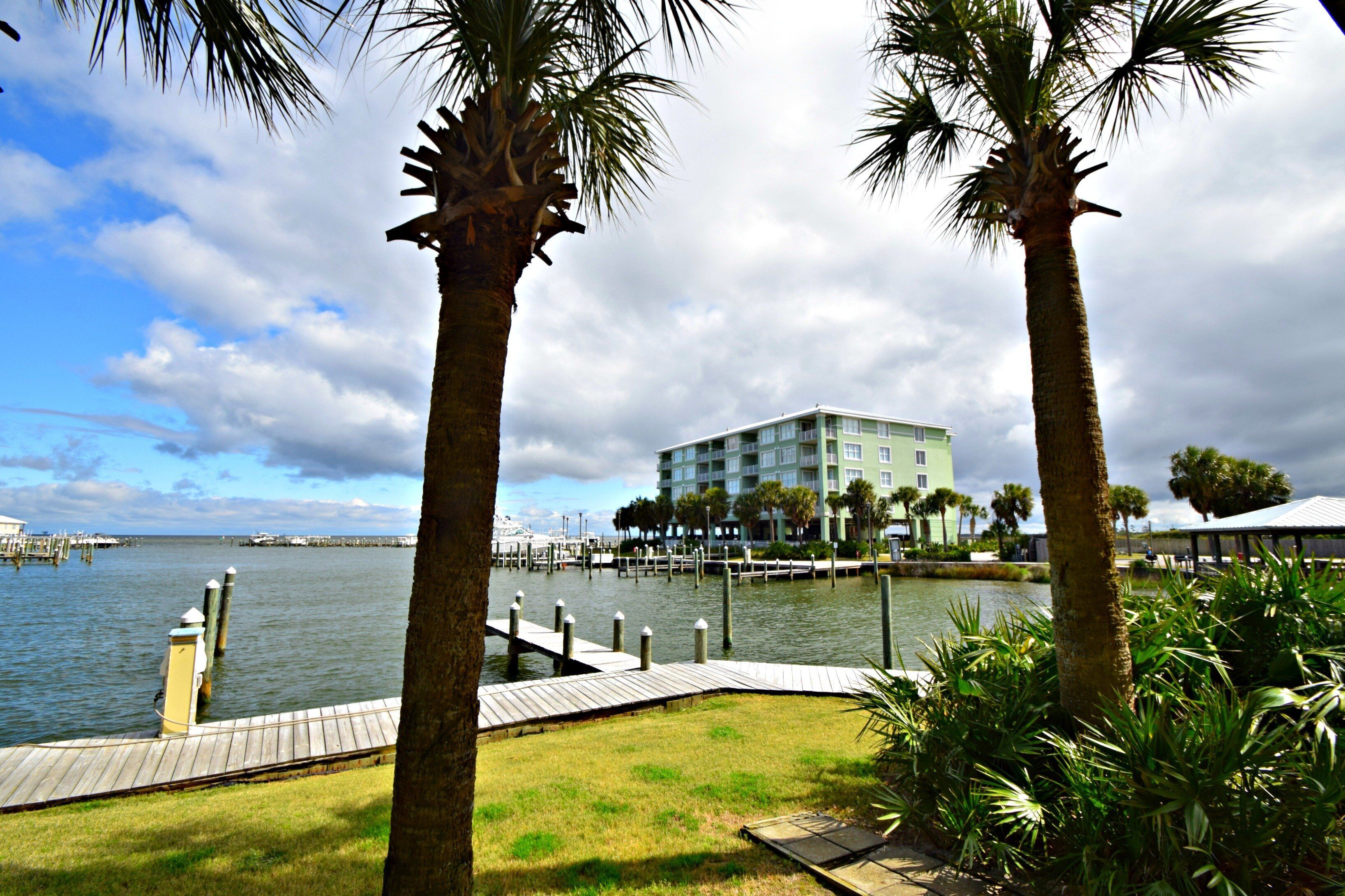 Hotel frente al mar con muelle, palmeras y un edificio con balcones con vistas al agua.