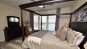 Un lit à baldaquin avec une couvre-lit à motifs, un fauteuil en cuir marron, une commode en bois foncé et une grande fenêtre avec des rideaux.