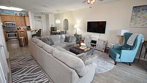 Un salon moderne avec un canapé d’angle, un fauteuil turquoise, une table basse et un téléviseur.