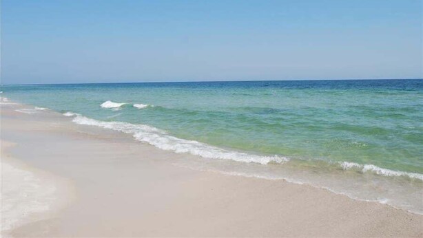 Une plage avec une eau d’un bleu limpide et un rivage sablonneux.