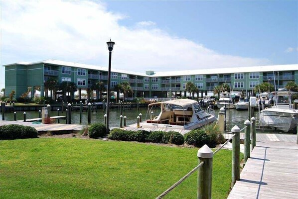 A marina with boats docked, a grassy area, and a building with multiple balconies. - Navy Core Harbor (Gulf Shores)