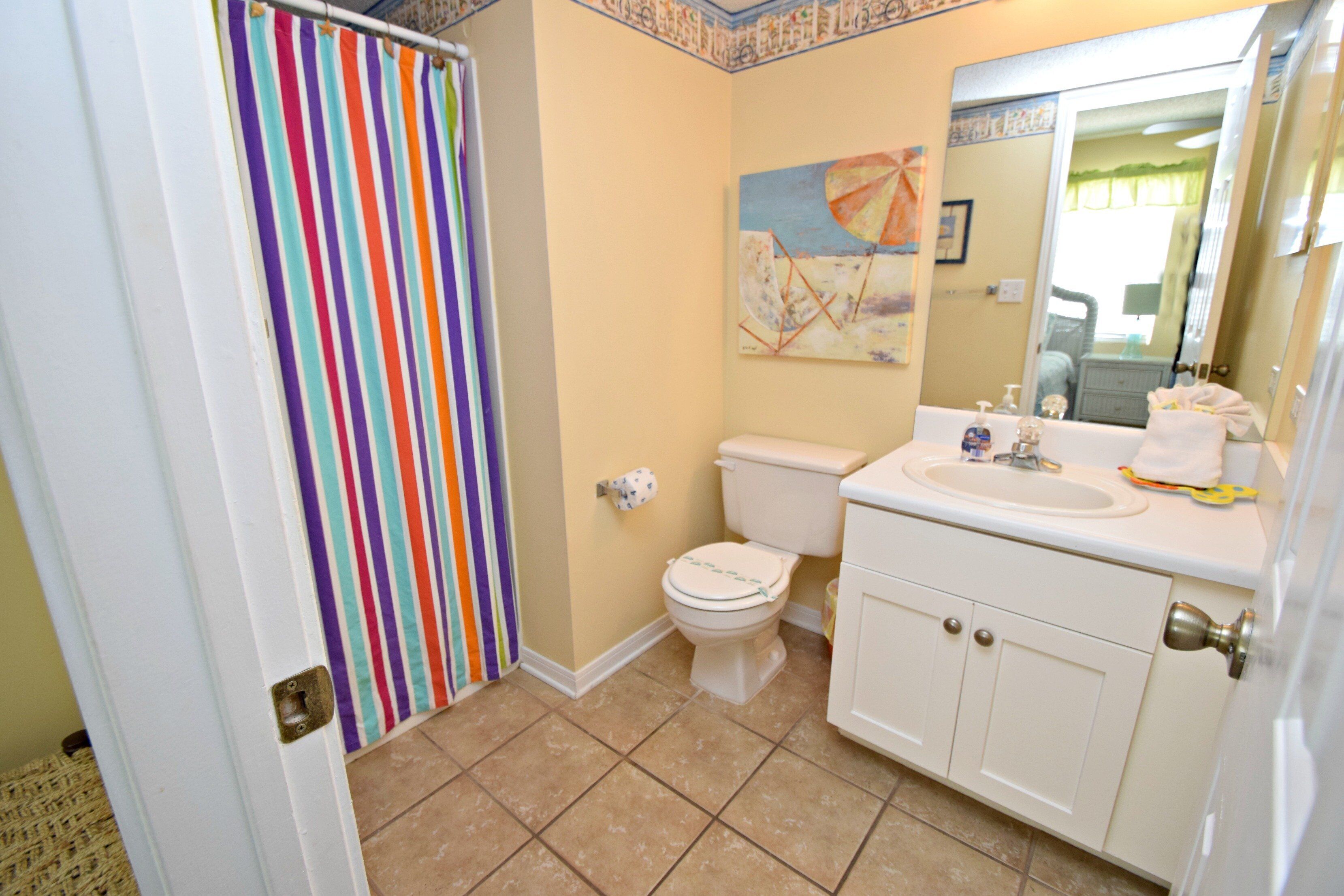A bathroom with a striped shower curtain, a toilet, a sink with a mirror, and a painting on the wall.