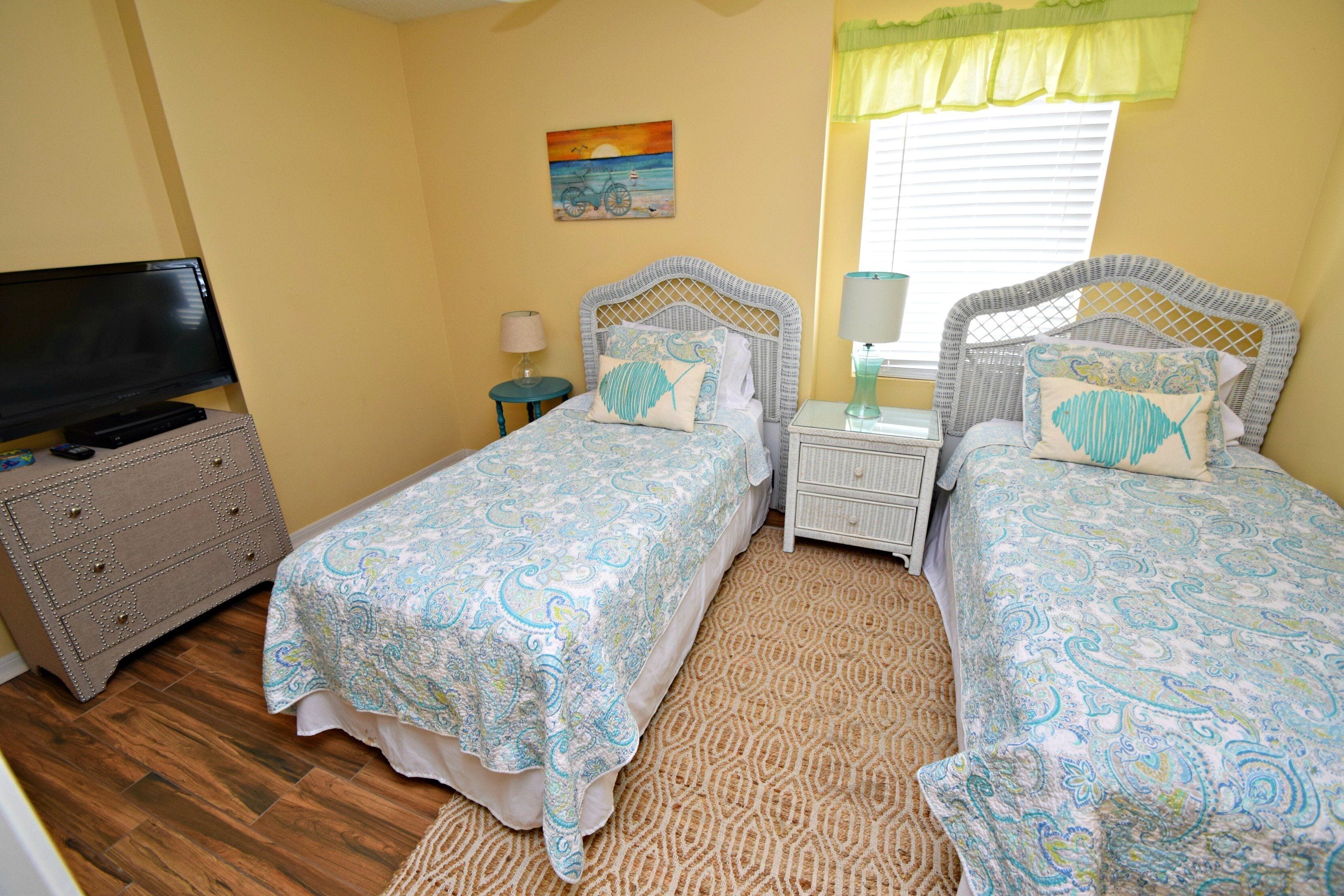 A bedroom with two single beds, a television, a dresser, and a painting on the wall.