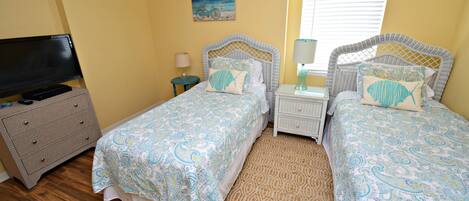 A bedroom with two single beds, a television, a dresser, and a painting on the wall.