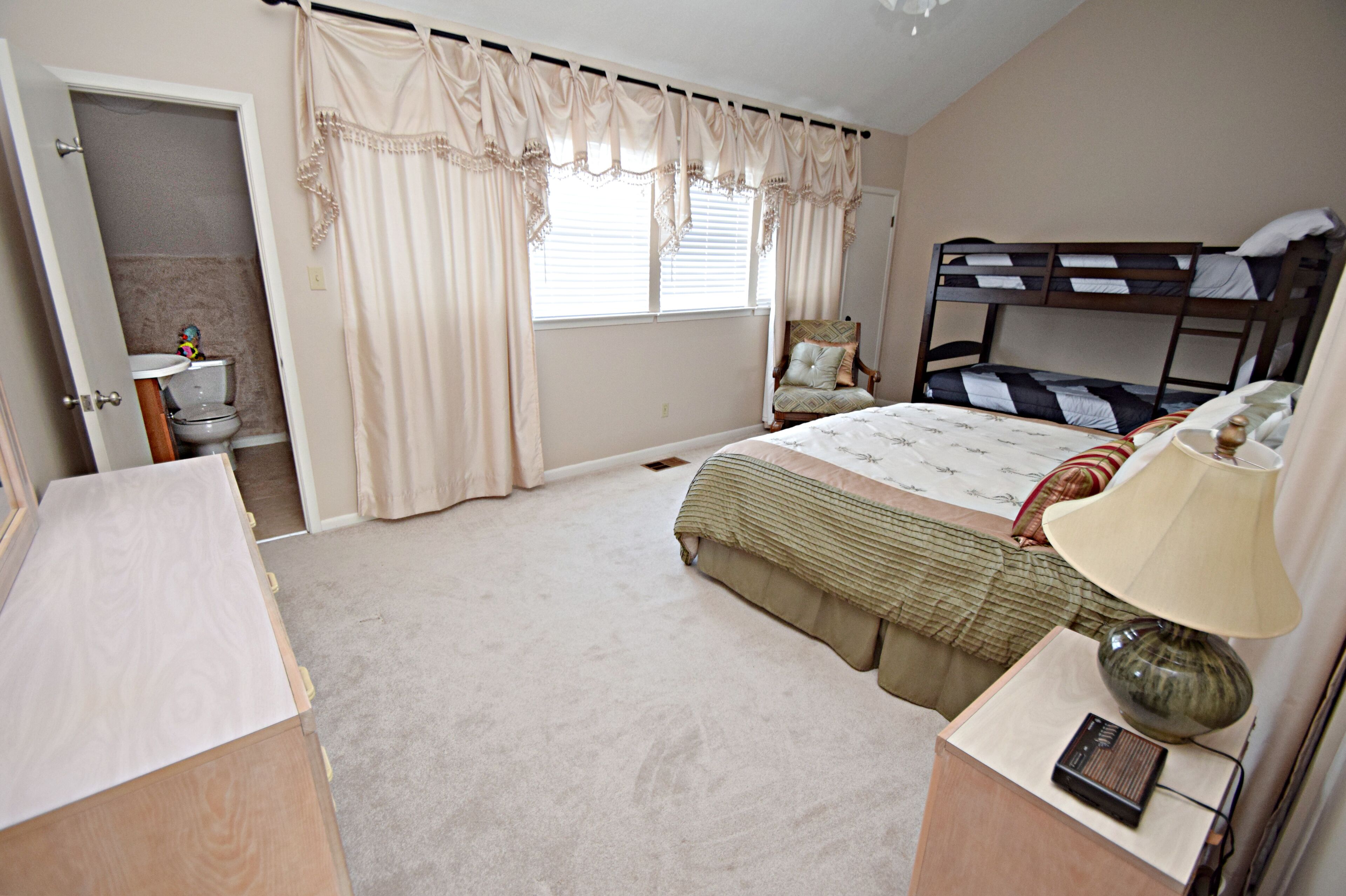 Une chambre avec un lit superposé, une table de chevet avec une lampe, une chaise et une salle de bain avec des toilettes et un lavabo.