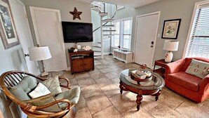 A living room with a television, wicker chair, red sofa, and a glass coffee table. - Ocean Reef (Gulf Shores)