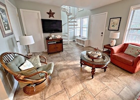 A living room with a television, wicker chair, red sofa, and a glass coffee table.