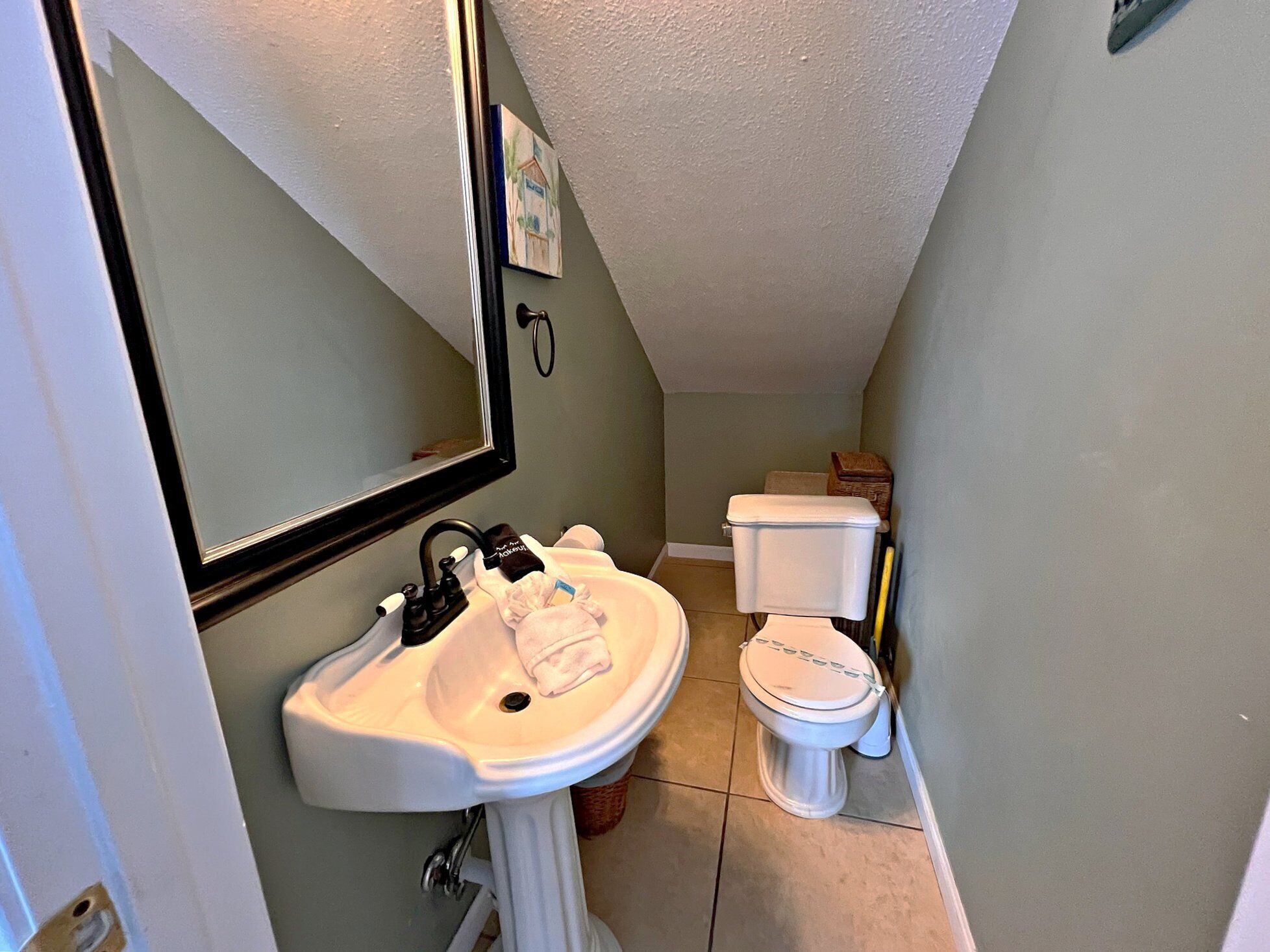 A small bathroom with a white sink, a mirror, a toilet, and a framed picture on the wall.