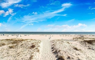 A beach with a clear sky, sandy dunes, and a pathway leading to the water.