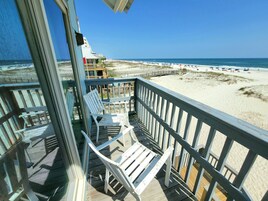A beach view from a balcony with white chairs and a wooden deck.