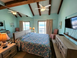 A bedroom with a bed, a desk, a chair, a TV, and a window with a view.