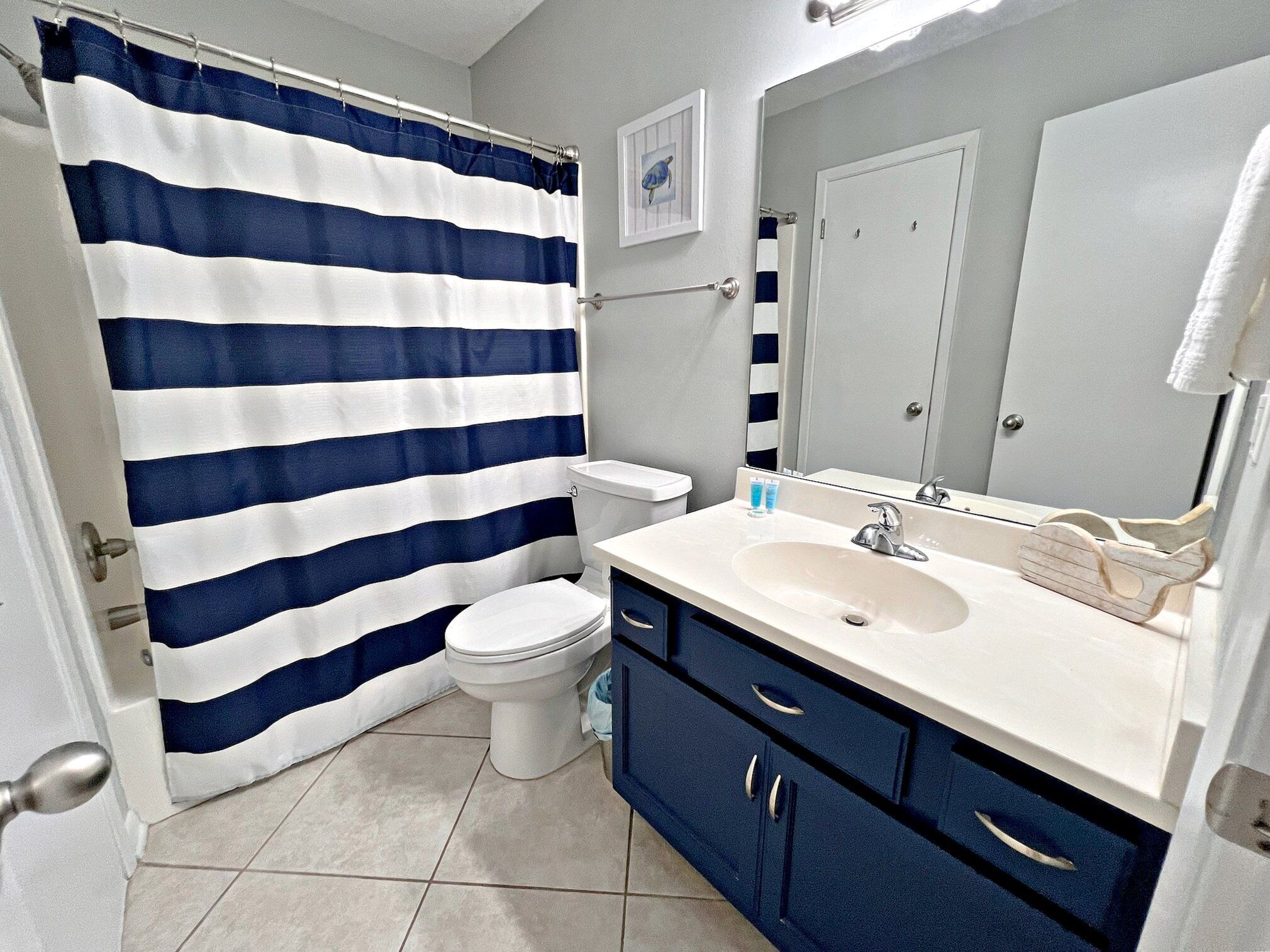 Une salle de bain avec un rideau de douche à rayures, des toilettes, un lavabo avec un miroir et des placards.