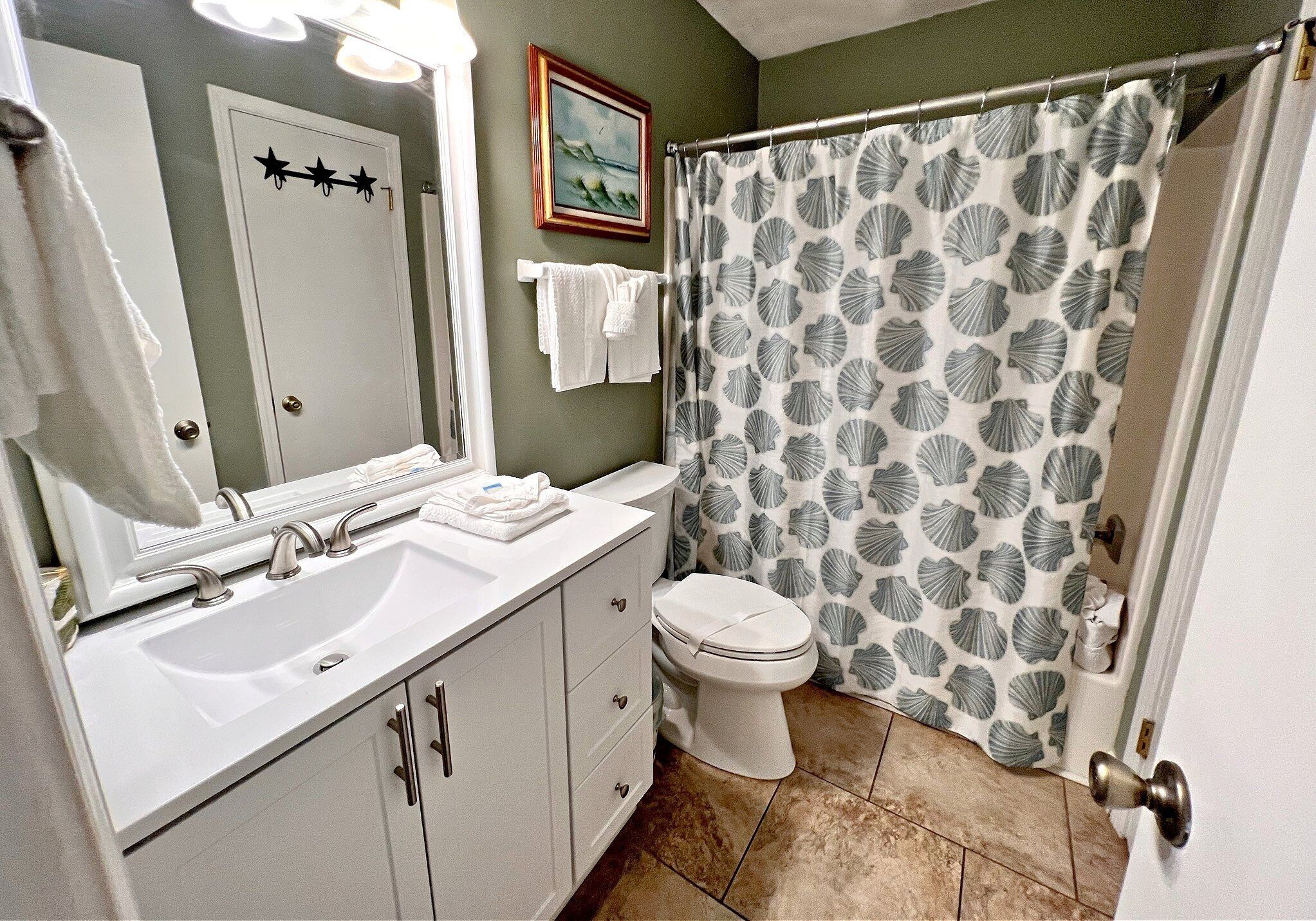 A bathroom with a white sink, a toilet, and a shower curtain with a shell pattern.