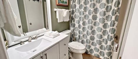 Baño con lavamanos blanco, inodoro y cortina de ducha con estampado de conchas.