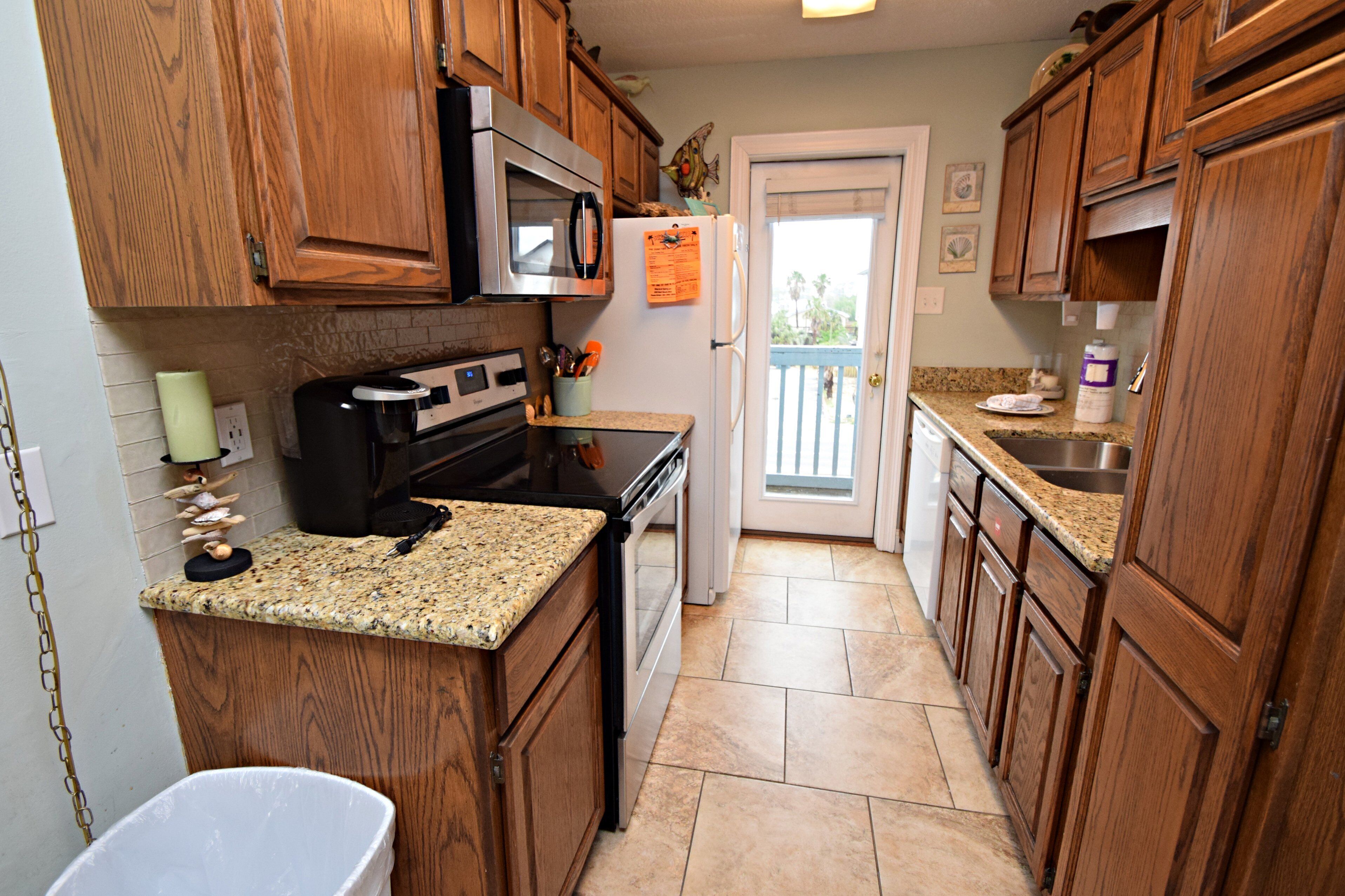 A kitchen with wooden cabinets, a stainless steel refrigerator, a microwave, a stove, and a granite countertop.