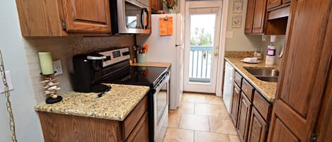 A kitchen with wooden cabinets, a stainless steel refrigerator, a microwave, a stove, and a granite countertop.