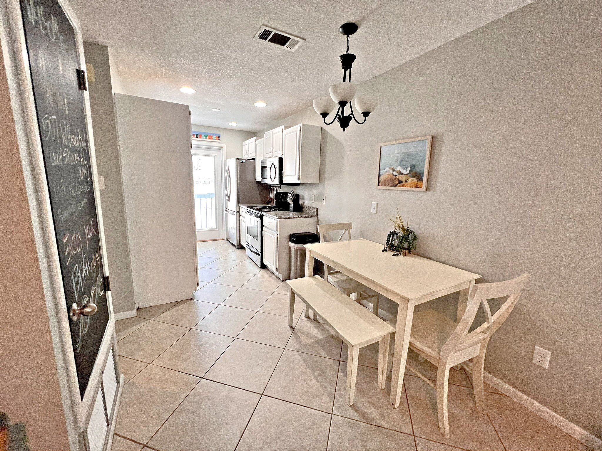 A kitchen with white cabinets, a dining table with benches, and a chandelier.